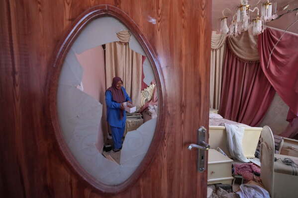 Mahasen Faqih is seen through a shattered glass door as she checks her home, destroyed during the Israeli military operation, after returning to it in Zawtar al-Gharbieh, Lebanon, Tuesday, July 28, 2026. (AP Photo/Hassan Ammar)