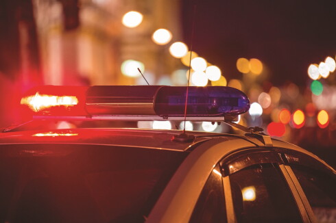 Stock art of red and blue emergency lights atop a police vehicle with the lights of a city street blurred in the background.