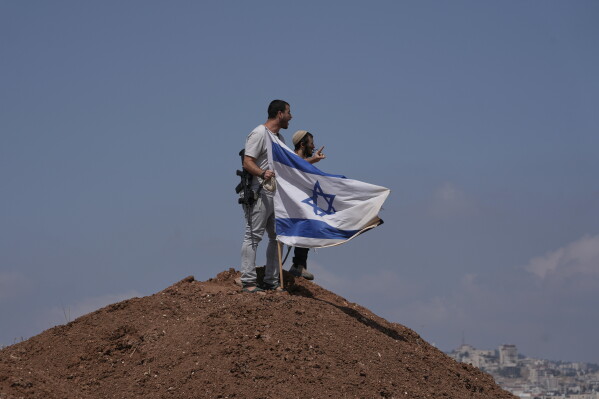 Israeli settlers put up an Israeli flag on a hilltop after it was taken down by Israeli and foreign peace activists during a protest in support of local landowners whose property is threatened with seizure by settlers, on the outskirts of the West Bank city of Beit Sahour, Friday, Aug. 14, 2026. (AP Photo/Mahmoud Illean)