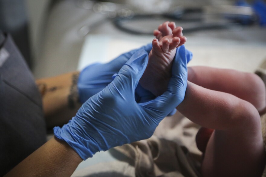 A midwife checks a baby's feet after birth in this file photo. Only the midwife's gloved hands and the baby's feet and legs are visible.