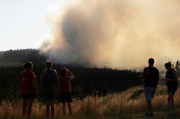 People watch Old Trails Fire from W. Northwest Blvd., Saturday, Aug. 1, 2026, in Spokane, Wash. (AP Photo/Young Kwak)