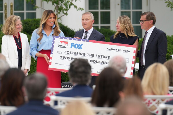 Fox Sports CEO Eric Shanks, center, and IndyCar President Doug Boles, right, present a commemorative check to first lady Melania Trump, second left, to fund her scholarship initiative "Fostering The Future," as Indiana University President Pamela Whitten, left, and Cherise Hall, vice provost for enrollment management at Purdue University, second right, look on an event in the Rose Garden of the White House, Thursday, Aug. 20, 2026, in Washington. (AP Photo/Jacquelyn Martin)