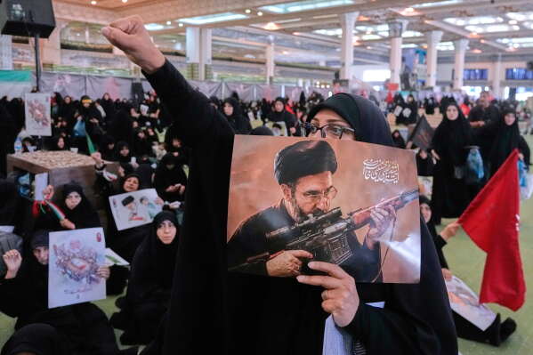 A mourner chants slogan as she holds a poster with graphic depicting Iran's Supreme Leader Ayatollah Mojtaba Khamenei in a ceremony commemorating the late Supreme Leader Ayatollah Ali Khamenei at the Imam Khomeini Mosalla Grand Mosque in Tehran, Tuesday, July 14, 2026. (AP Photo/Vahid Salemi)