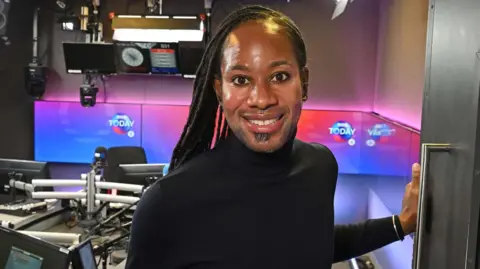 BBC Dressed in a black turtle neck and trousers, Jason Arday smiles at the camera in a BBC Radio 4 studio.