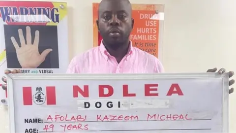 NDLEA Afolabi Kazeem Micheal holds up a NDLEA sign with his name and age after his arrest in Lagos