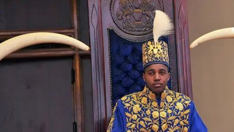AFP via Getty Images King Oyo pictured at 18 during his coronation wearing a gold embroidered jacket and hat.