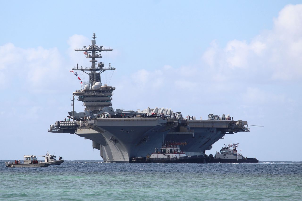 Harbor tug boats guide Nimitz-class aircraft carrier USS Abraham Lincoln at the naval base in Guam on December 11, 2025.
