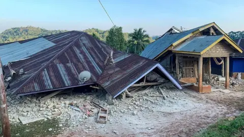 Getty Images A house has collapsed so that only the roof is visible, lying on the ground.