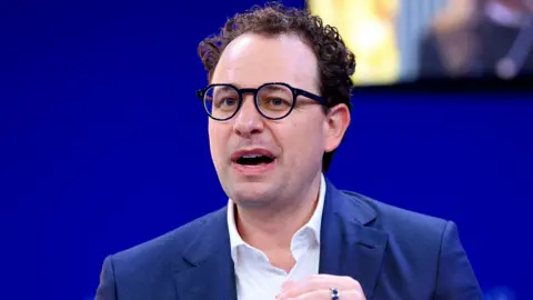 Reuters Anthropic CEO Dario Amodei speaking on a stage while gesturing with his hands.