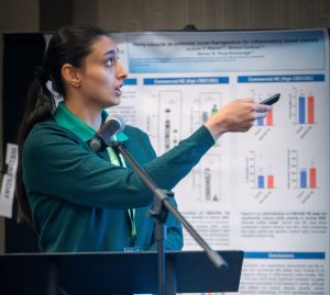 A woman stands at a podium holding a remote, pointing it toward a projector screen.