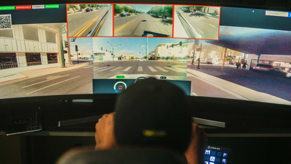 Back view of a remote driver in front of a screen delivering a car to a location.