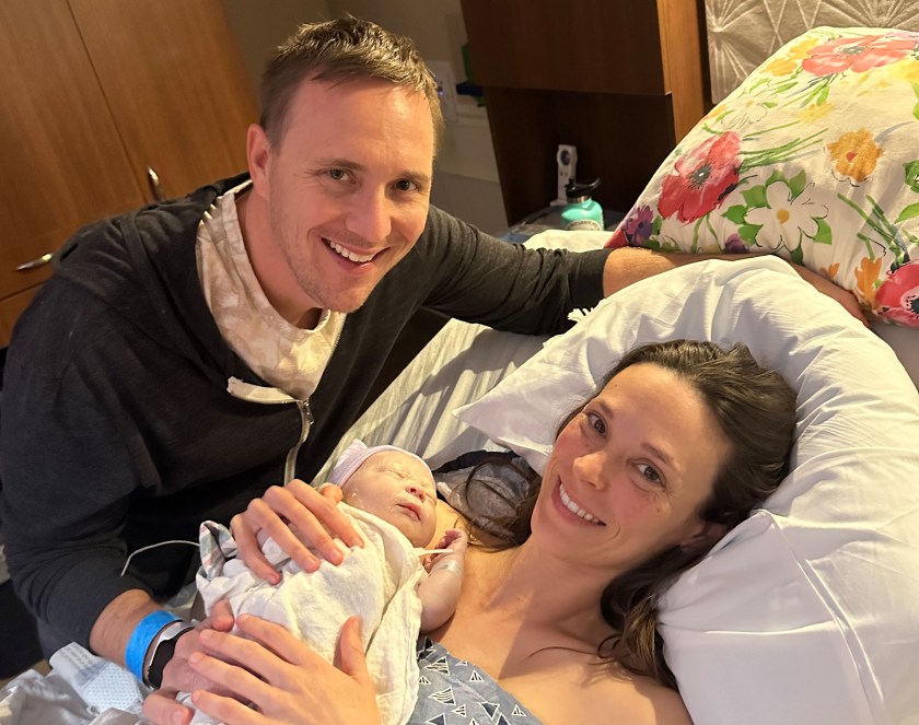 A photo of Emilie Solomon in a hospital bed. She holds her newborn son in her arms. Her husband, Justin, is by the bed.