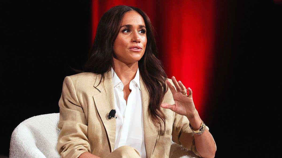 Meghan Markle in a biege and white pantsuit speaking on stage in New York City.