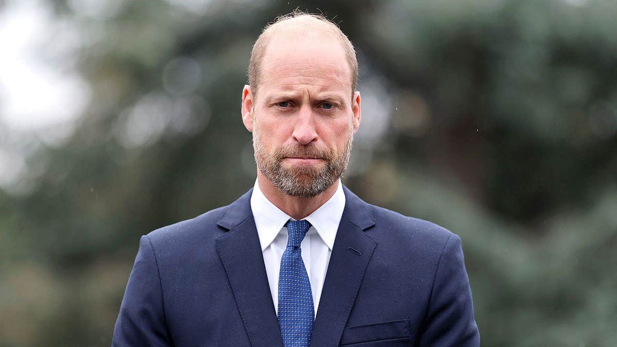 Prince William looking serious in a dark blue suit.