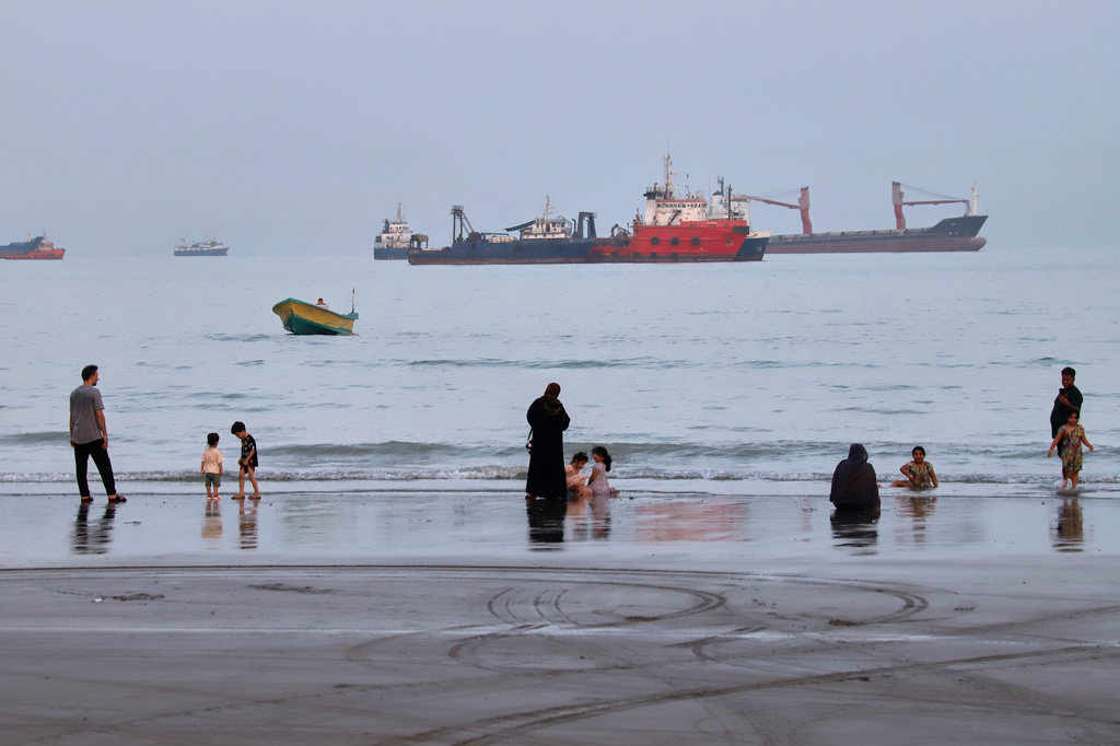 People spend time at a beach as commercial vessels are anchored in the Strait of Hormuz off Bandar Abbas, Iran, Wednesday, Aug. 5, 2026.