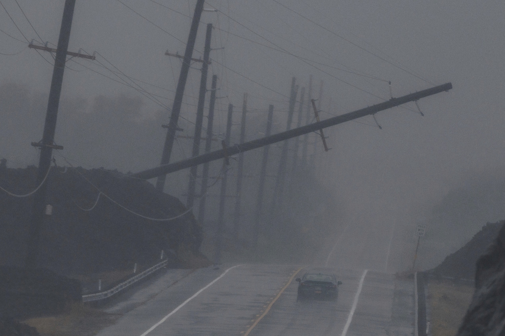 A vehicle drives near a downed utility pole dangling above Mamalahoa Highway during Hurricane Lala near Ocean View, Hawaii, Saturday, Aug. 15, 2026.