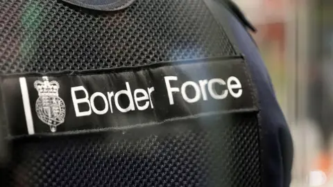 BBC A stock image of a person wearing a UK Border Force vest. Is it a close up picture of the writing on the front.