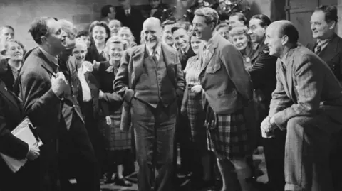 Getty Images A black and white image showing Roger Livesey, in a kilt, and Michael Powell, seated, as the cèilidh scene is recorded in I Know Where I'm Going.