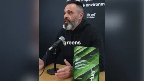 Advertising Standards Authority A screengrab of the banned advert on Instagram featuring a still of Julian Hearn speaking into a microphone with a bag of the product on the table next to him. Hearn has a mid-length black beard, streaked with grey and short dark hair. He has brown eyes and wears a black hoodie.