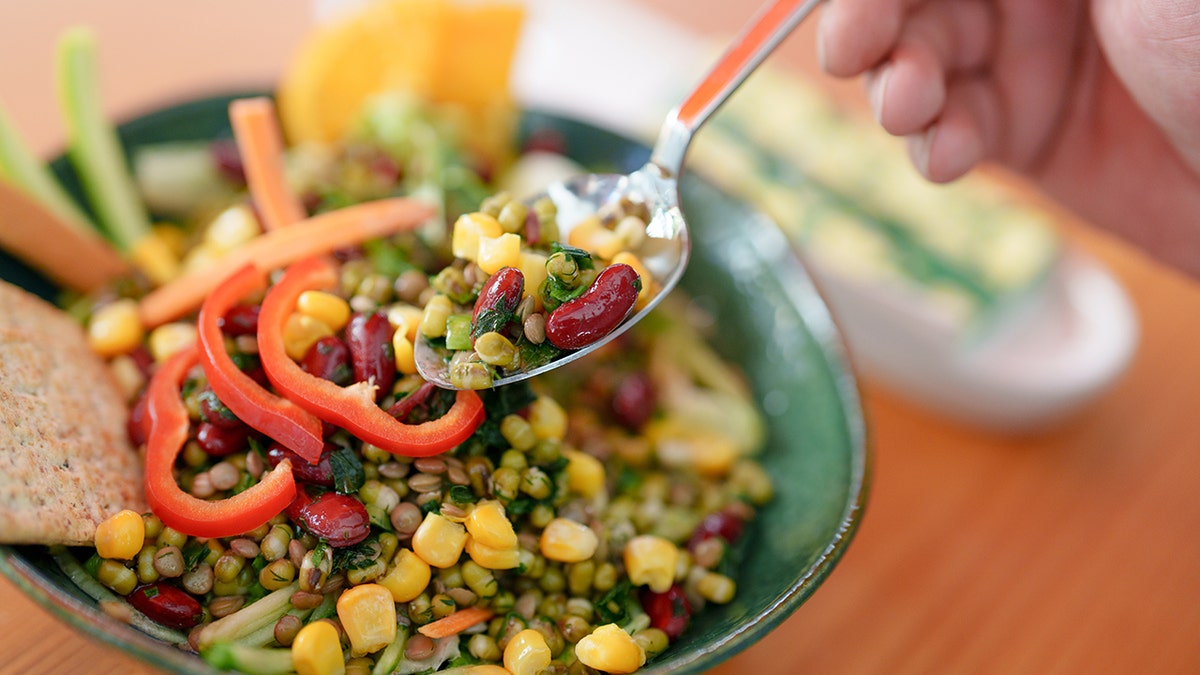 Beans and corn are shown on a spoon in hand.