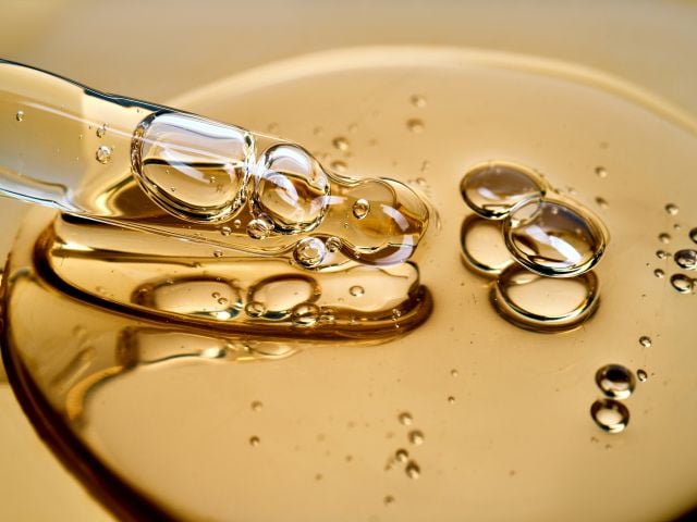 Photograph of a glass dropper releasing golden viscous oil with air bubbles