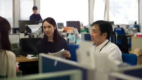 Getty Images A posed scene from a Japanese office, with three workers having a meeting