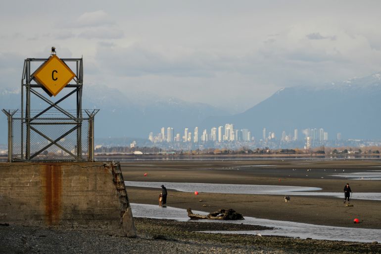 People walk on the Canadian side of Maple Beach during low tide, with the international boundary line marked by a cement tower at left, as seen from Point Roberts, Washington, the United States, on March 18, 2025