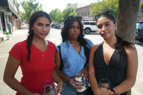 Eloise Alanna Three 21-year-old women stand holding cupcakes just purchased in a shop on one of Kingsport's main streets downtown. One wears a red V-neck top, cross necklace and her long, dark hair in a braid. The friend next to her wears sunglasses atop her head and a blue v-neck top above jeans. The third, her hair in a ponytail, wears a black halter top and sunglasses atop her head