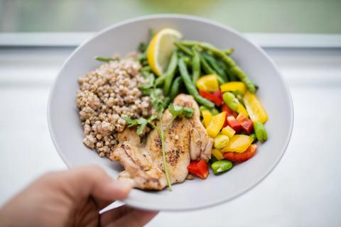 Hand holding a plate filled with grilled chicken breast, veggies and buckwheat