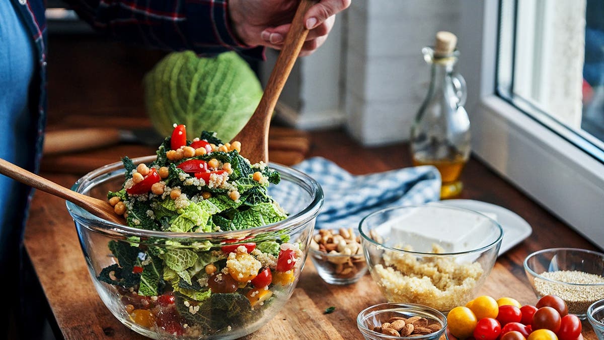 A person mixes a salad that contains chickpeas.