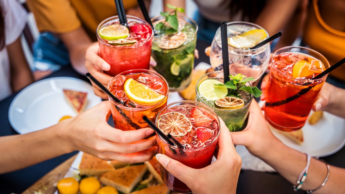 Cheerful friends enjoy happy hour at a restaurant as they toast their colorful drinks.