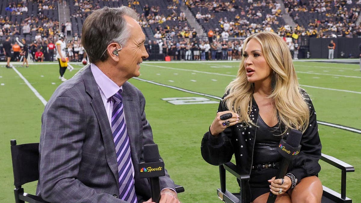 Cris Collinsworth and Carrie Underwood stand together before an NFL game at Allegiant Stadium.