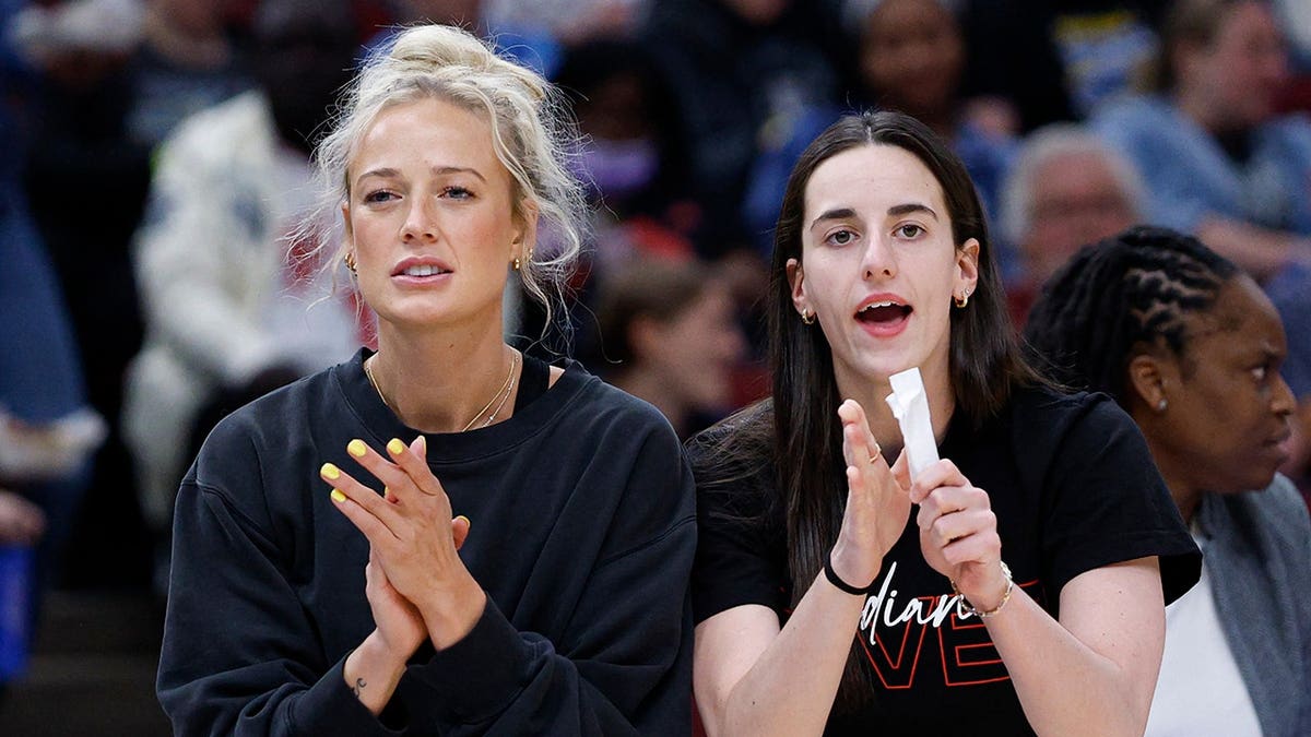 Sophie Cunningham and Caitlin Clark cheering from the Indiana Fever bench during a WNBA game, applauding and supporting their teammates from the sideline.