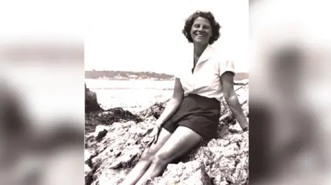 Supplied A black and white photo of a young woman in a white shirt and dark shorts sitting on some rocks.