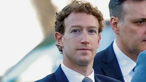 Reuters Meta CEO Mark Zuckerberg looking at a camera while walking into a Los Angeles courthouse, wearing a blue suit, tie and white shirt.