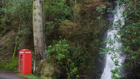 Getty Images A bright red phone box, sitting next to a waterfall