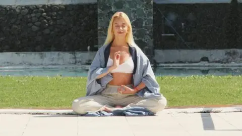 Anastasiia Mirraslavska Anastasia sits cross-legged meditating in a garden on a sunny day