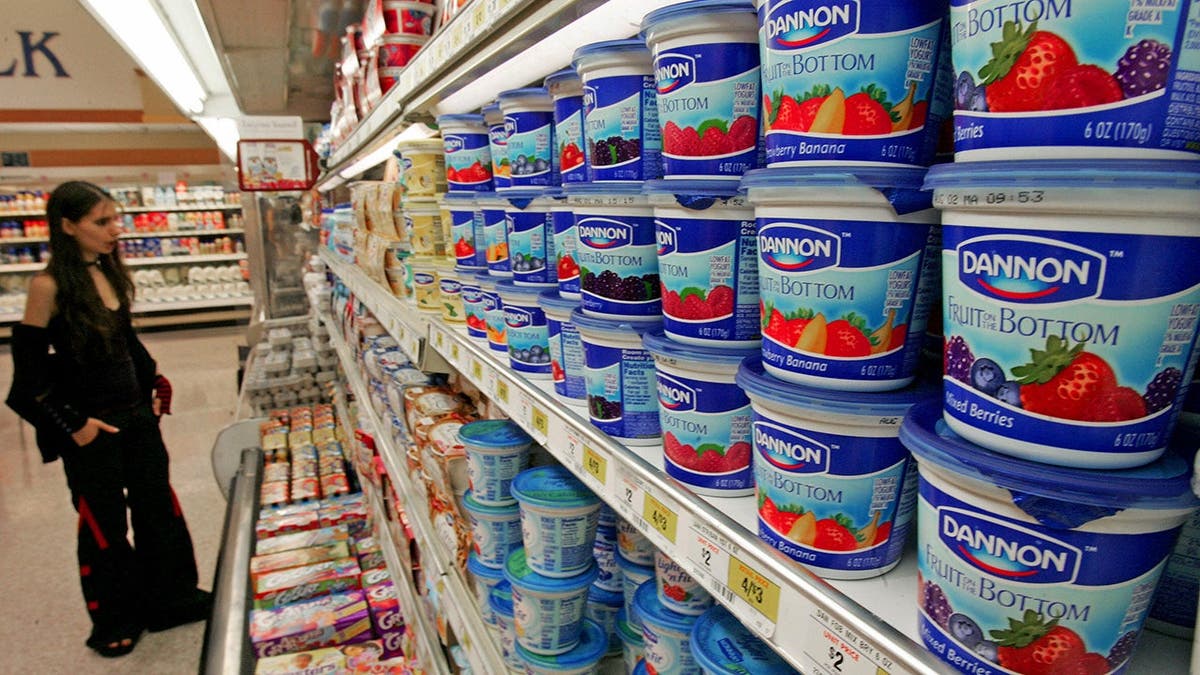 A woman stands in a grocery store looking at yogurt.