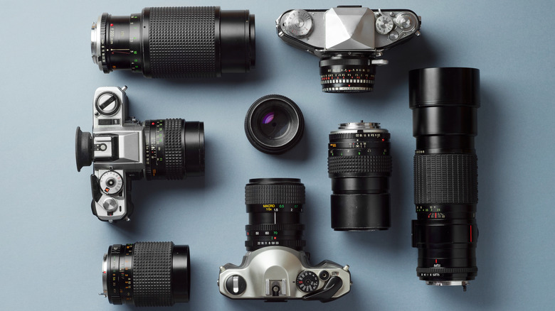 Top-down view of vintage cameras and camera lenses on a blue background.