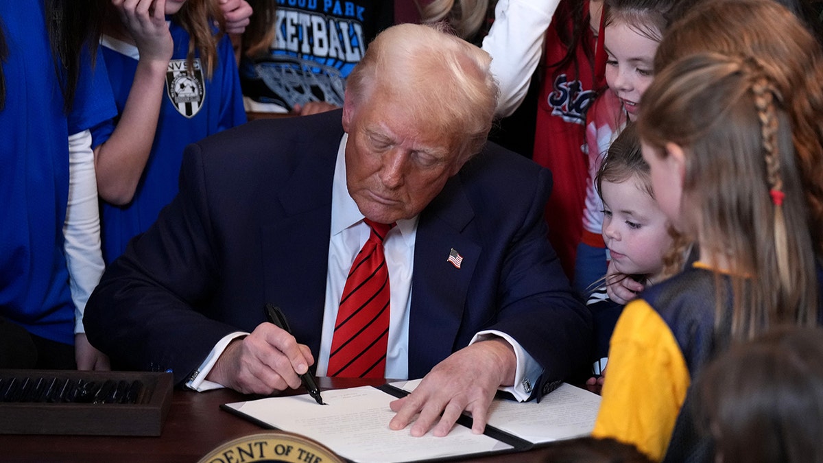President Donald Trump signs the order surrounded by female athletes