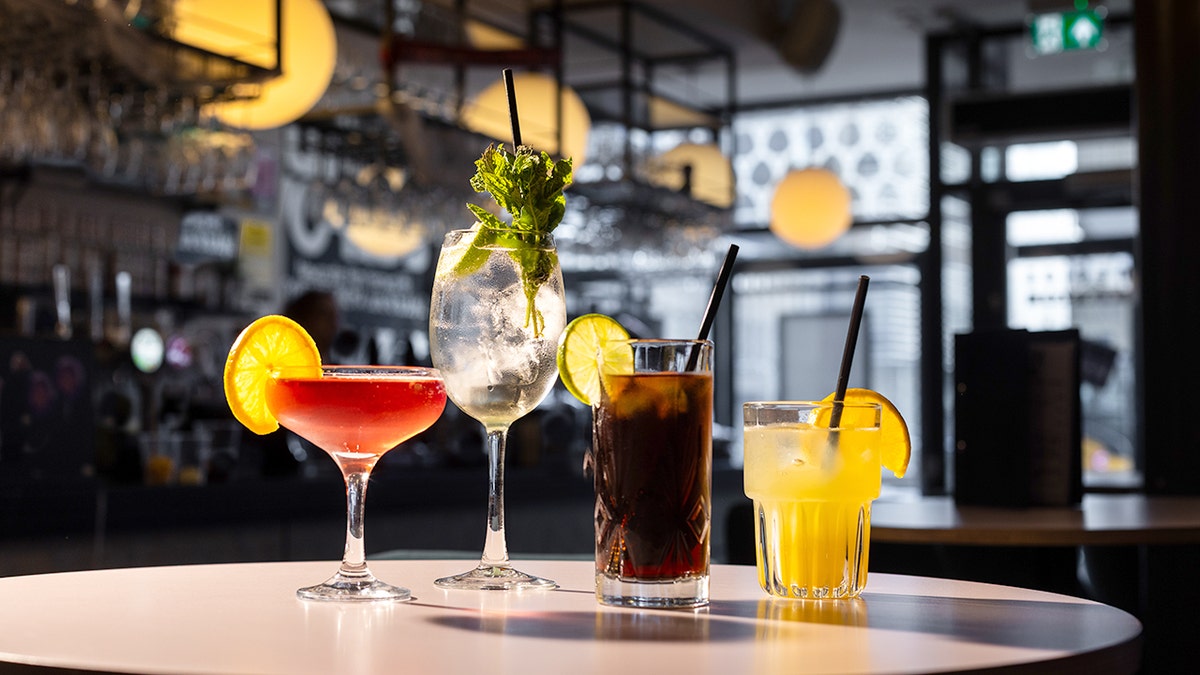Set on a high bar table are four colourful drinks in glasses of different shapes, some have straws, and some have fruit.