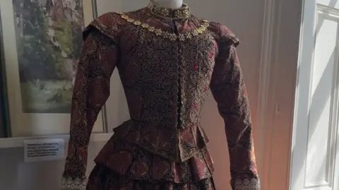 An ornate, burgundy dress with gold piping