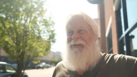 Eloise Alanna David Carter sports a full white beard - which helps him play Santa at Christmas - as he stands on a main street in downtown Kingstport