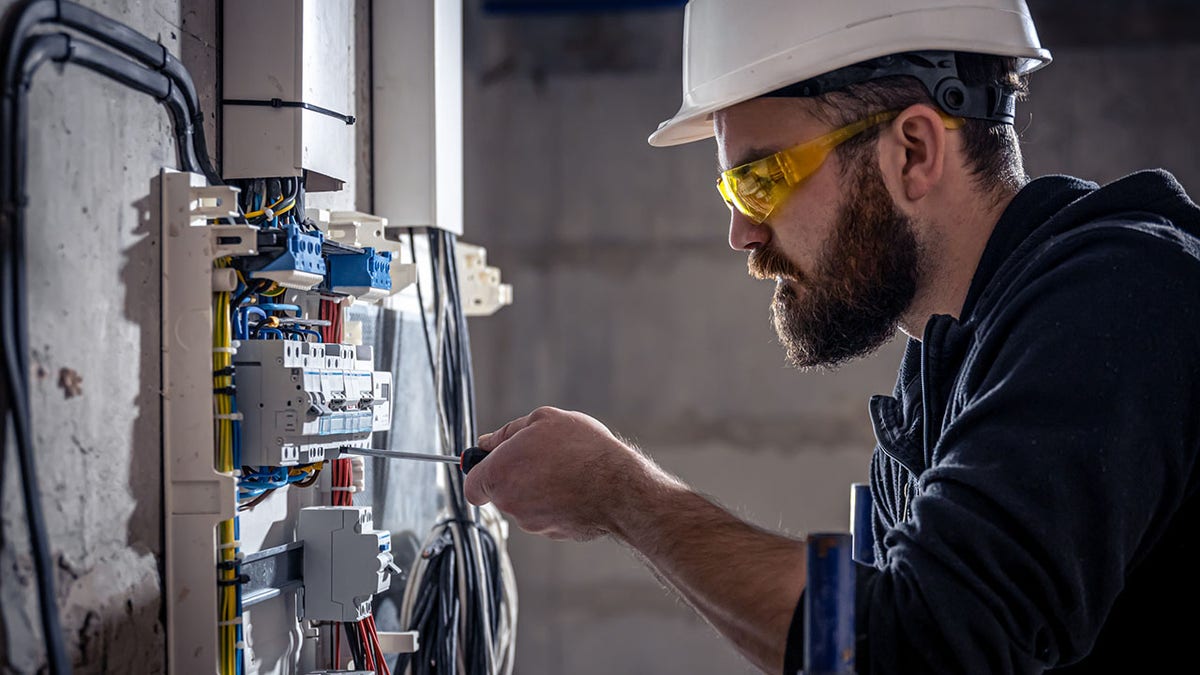 A male electrician works in a switchboard with an electrical connecting cable.