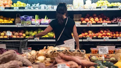 Getty Images A woman looks at apples in a supermaket aisle.
