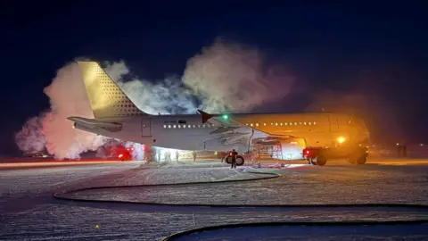 Supplied: Skytraders A large plane sits on the snow in the dark with clouds of vapour around it