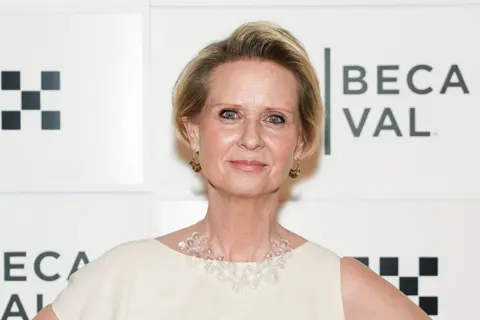 Getty Images Cynthia Nixon stands in front of a sign wearing a white gown