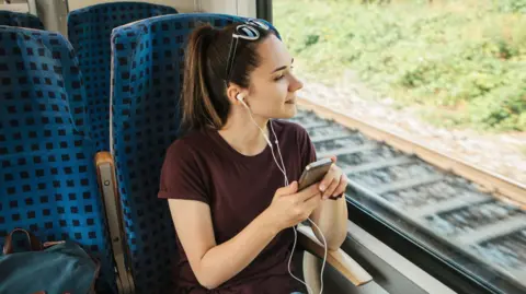 Getty Images A teenage girl sitting on a train listening to headphones