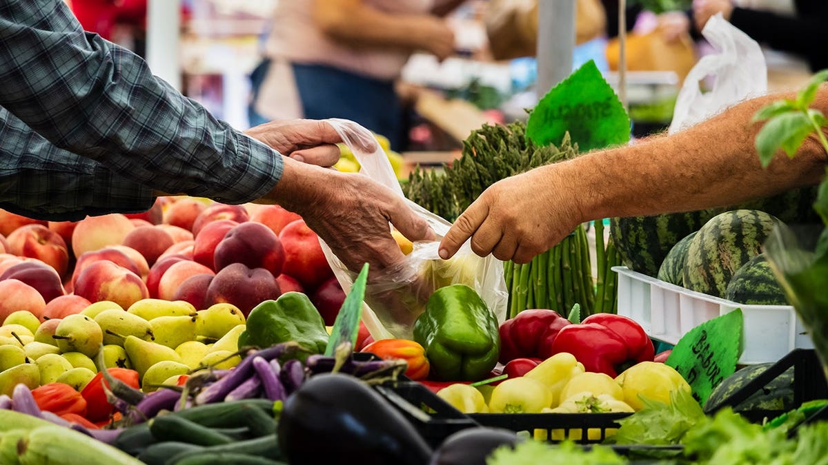 Buyer and vendor exchange fresh vegetables at a farmers market with colorful produce.