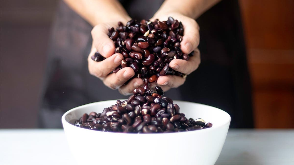 A person holds black beans in her hand above a heaping bowl of them.